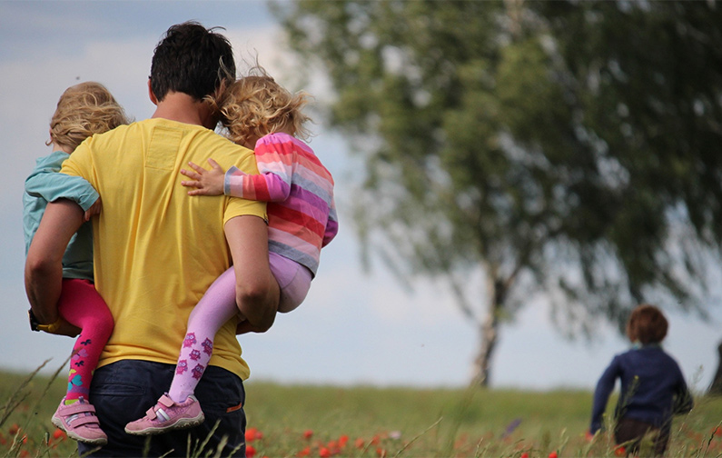 This is an image of a man spending time with his children in a meadow.