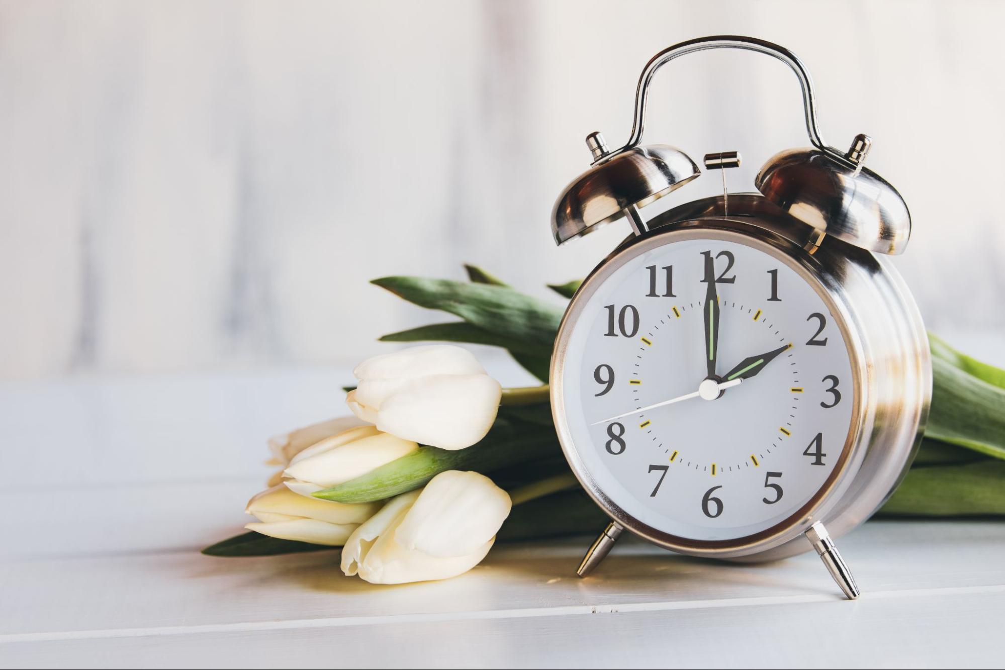 This is an image of a clock on a table with some tulips nearby.