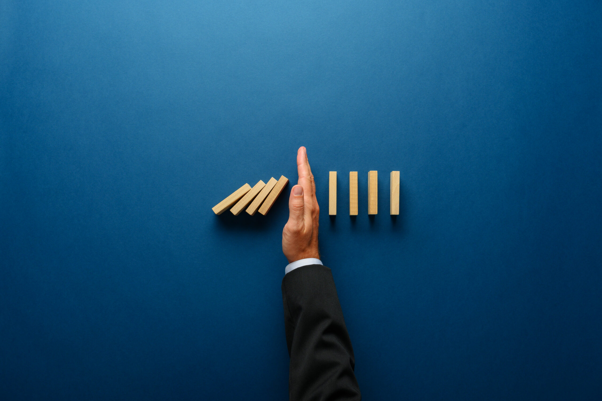 top,view,of,businessman,hand,stopping,falling,dominos,in,a